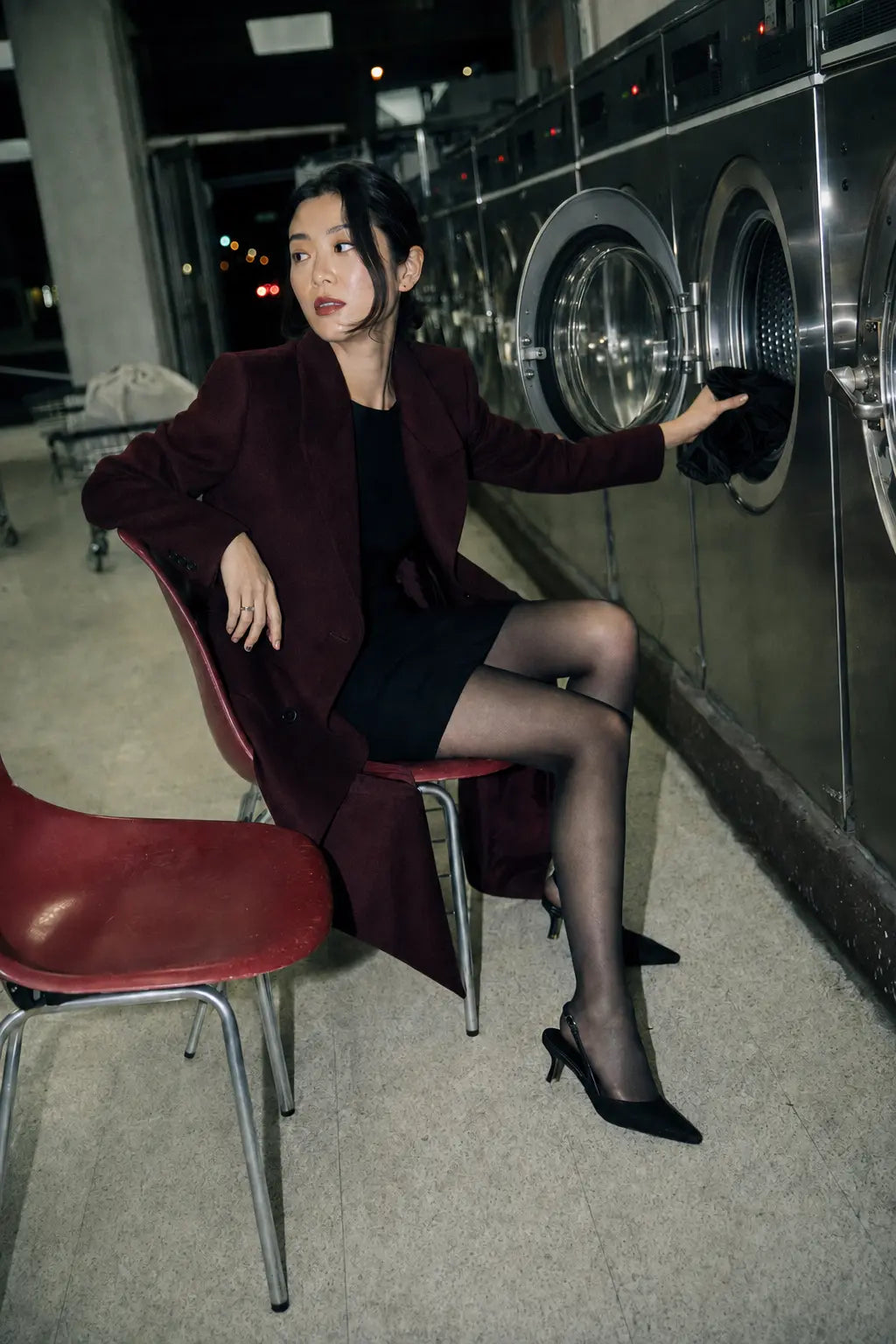 Model wearing black sheer Lorve Studio tights in a late-night laundromat